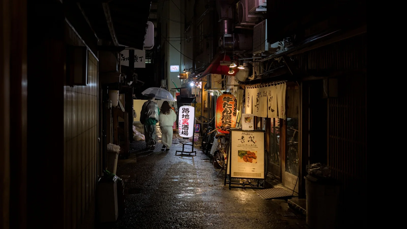 Rainy alley in Osaka with travelers walking under umbrellas